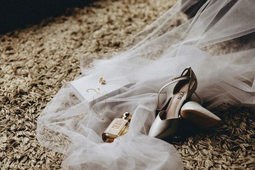 Free Close-up of bridal shoes, veil, and perfume on textured carpet for a wedding setup. Stock Photo