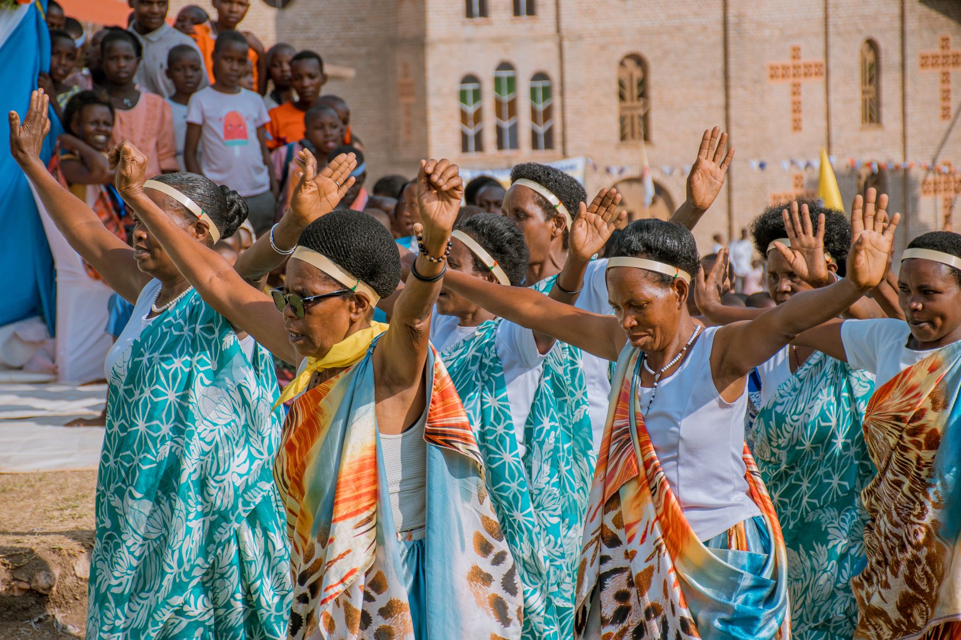 Women in traditional attire performing a cultural dance at an outdoor event with a lively crowd.