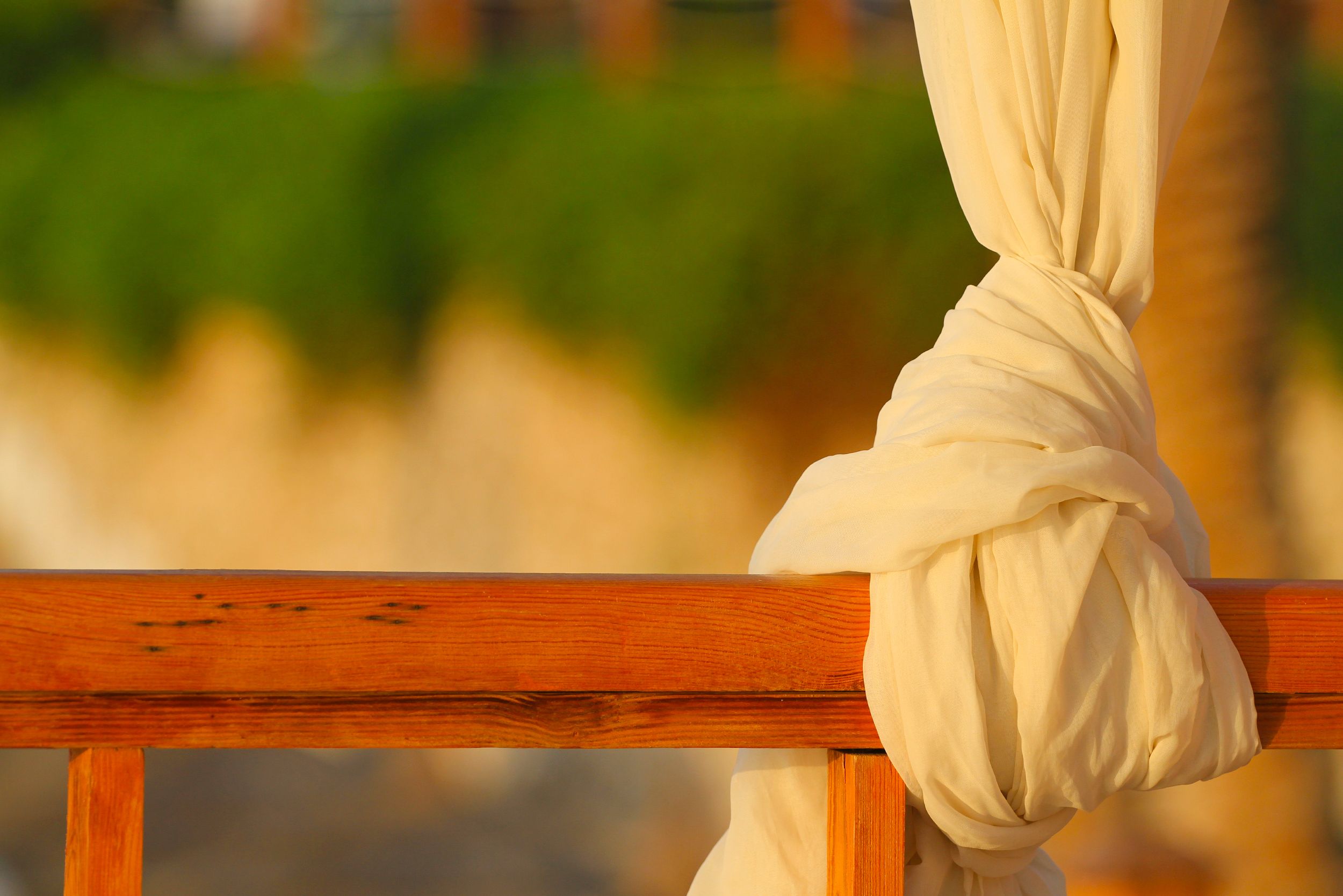 Close-up of cream-colored fabric elegantly draped over a rustic wooden railing outdoors.