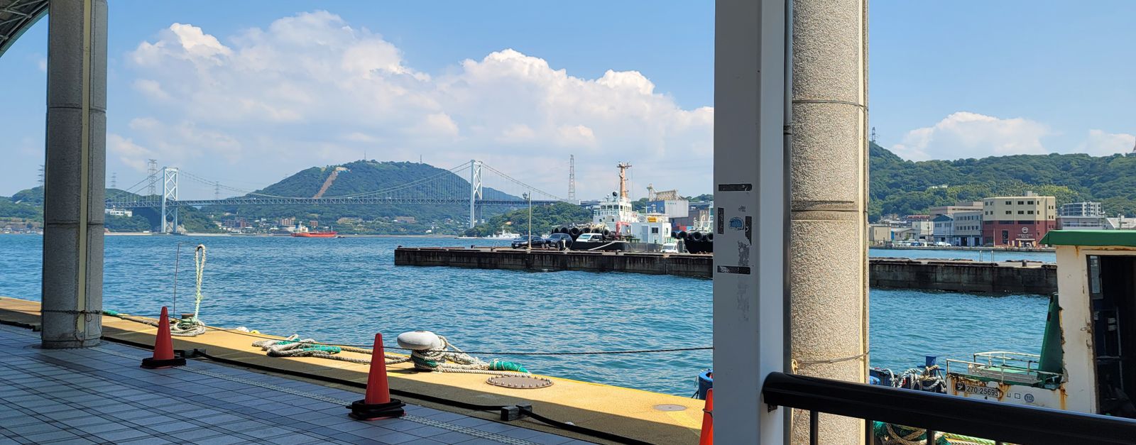 A scenic view from an industrial waterfront with a visible bridge and hillside under a bright blue sky.