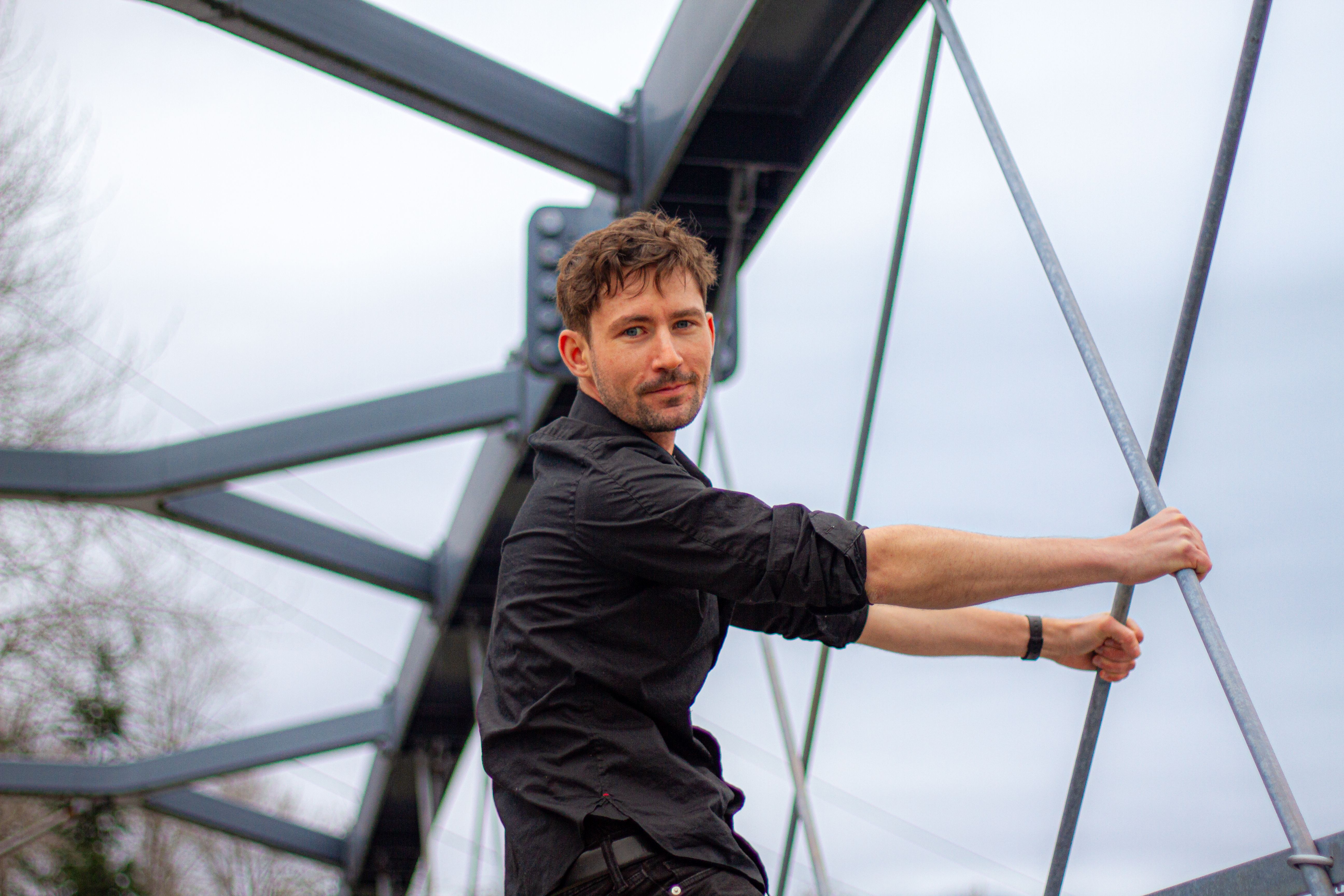 A confident man poses on a modern steel bridge in Vancouver, British Columbia.