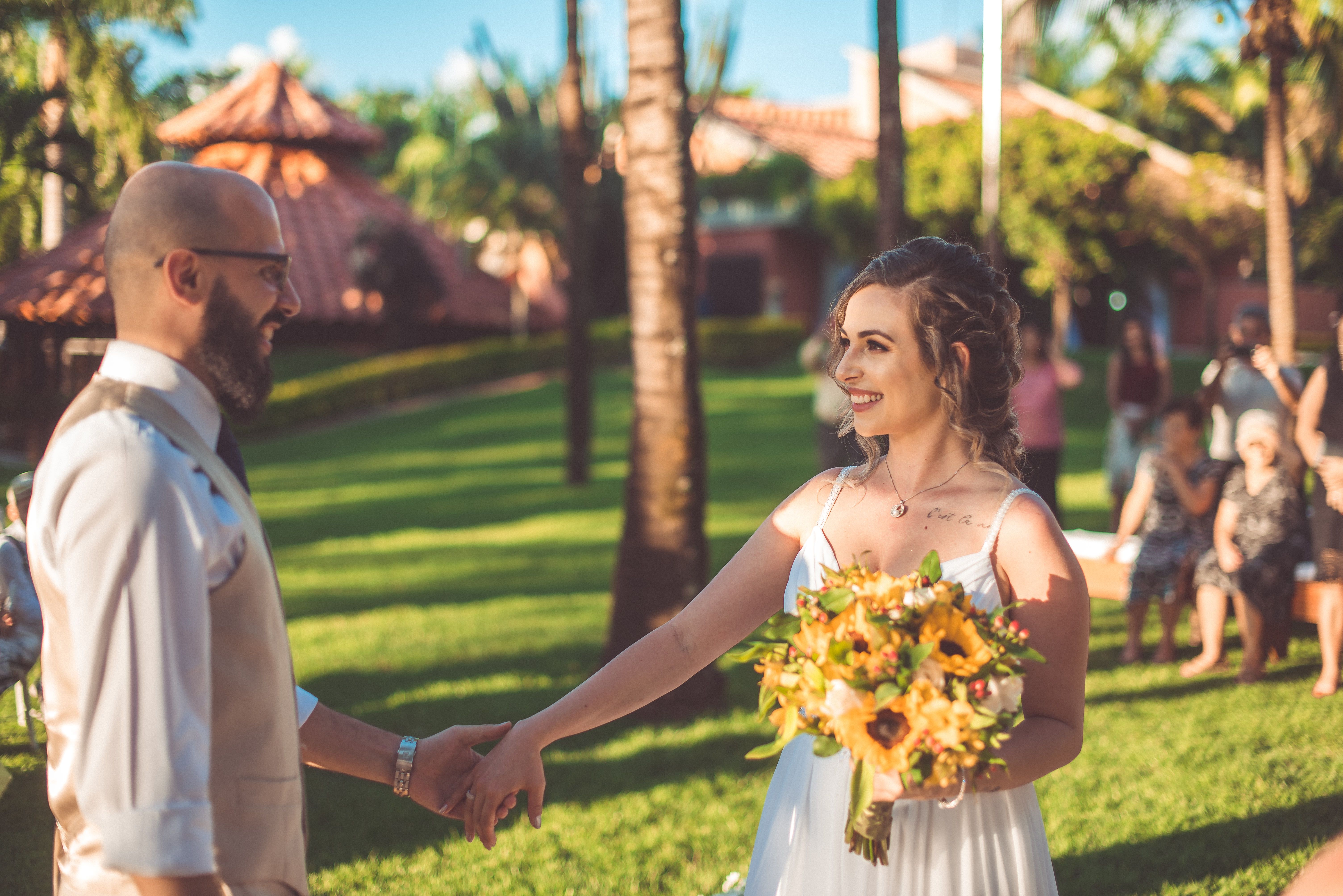 luxury wedding venues north coast egypt — A joyful bride and groom hold hands during a sunny outdoor wedding ceremony surroun