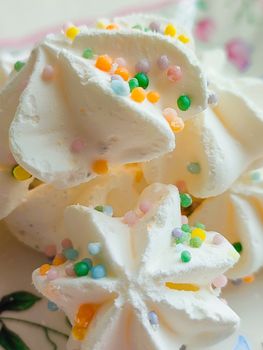 Close-up of meringue cookies adorned with colorful sprinkles on a floral plate.