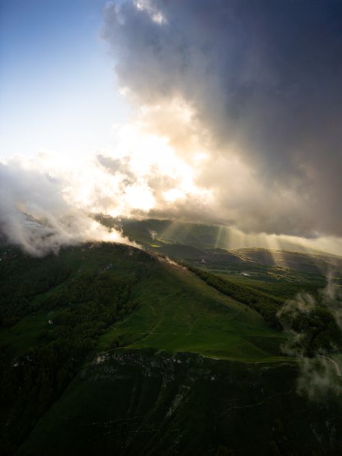 Free A breathtaking aerial view of a mountain range with sunlight breaking through dramatic clouds. Stock Photo