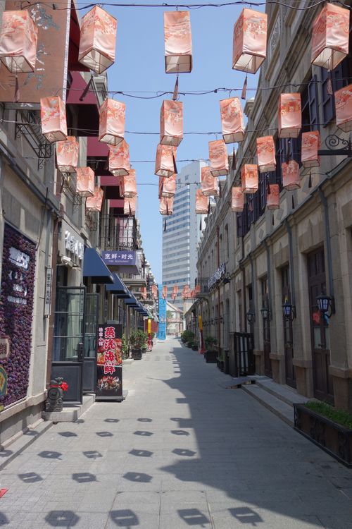 Free Colorful lanterns hang in a vibrant street leading to a tall modern building. Stock Photo