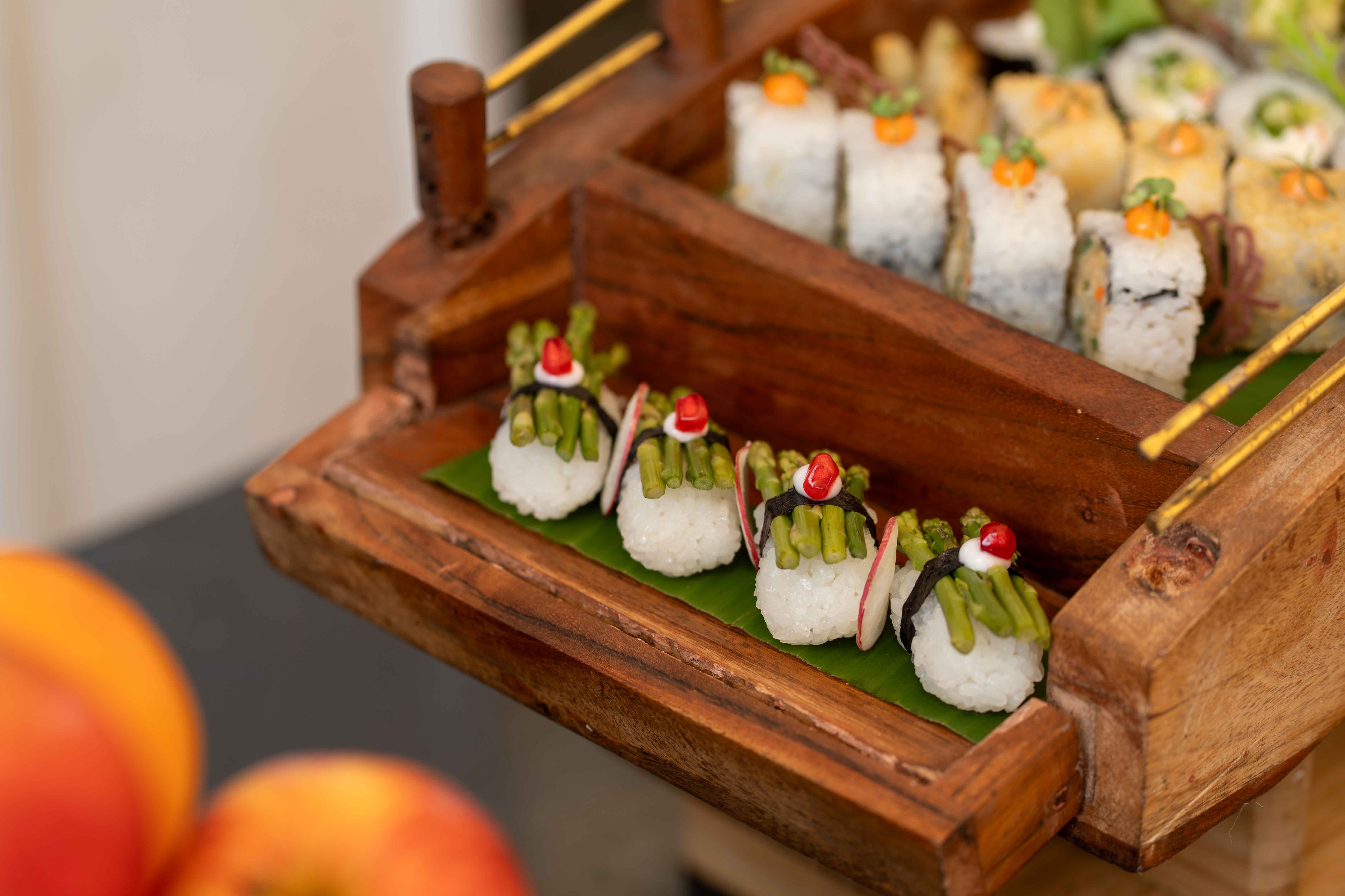 Colorful sushi rolls displayed on a wooden tray with a focus on asparagus and pomegranate toppings.