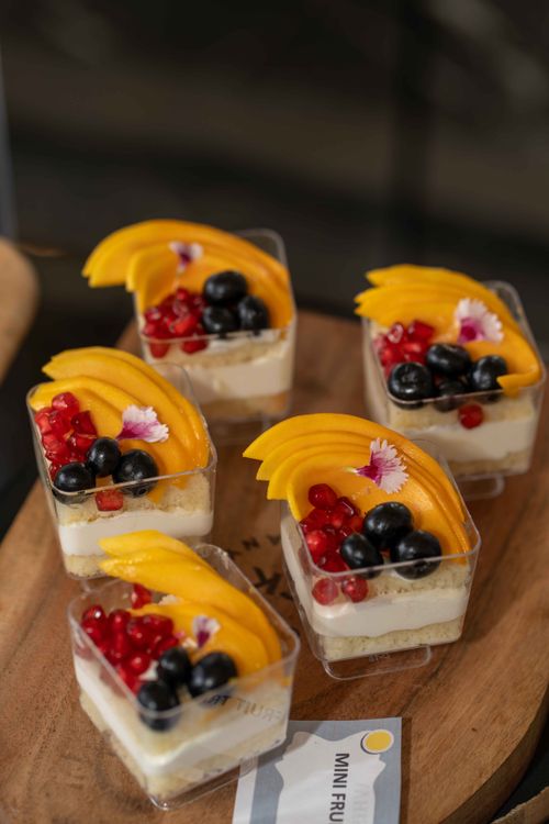 Free Five mini fruit cups with mango, berry, and flower garnish on a wooden platter. Stock Photo