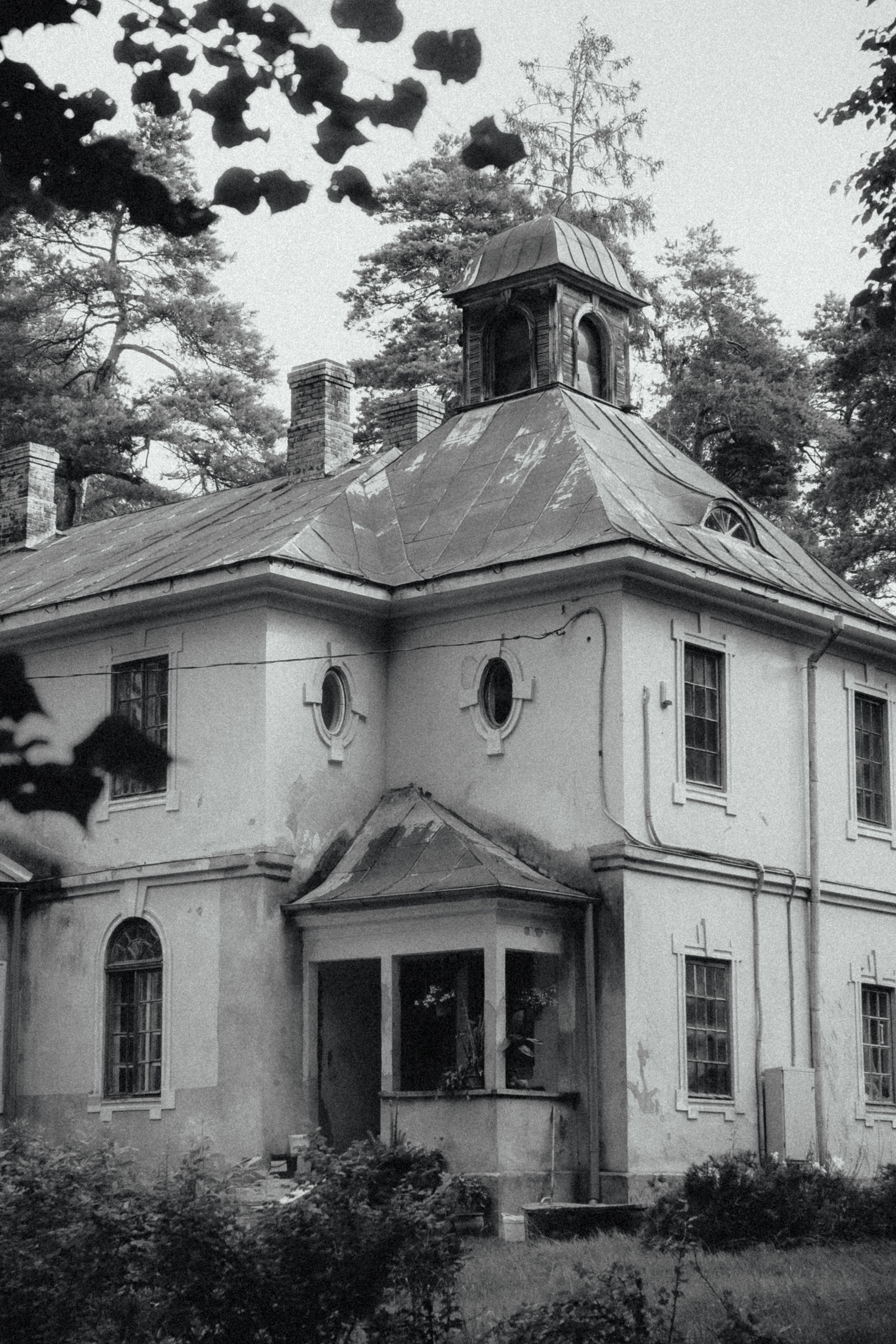 A weathered, abandoned historic mansion surrounded by overgrown woods, similar in style to a haunted house renovation project