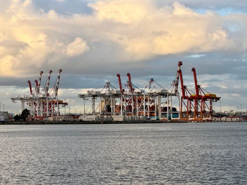 Free A wide view of an industrial port with cargo cranes under a dramatic sunset sky in Australia. Stock Photo