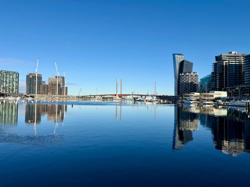 Free A crisp view of Docklands in Melbourne with clear reflections of buildings on the water. Stock Photo