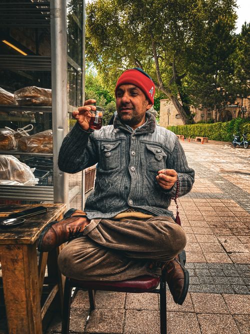Free A man in a winter jacket and hat drinking tea outside by a bakery display. Stock Photo
