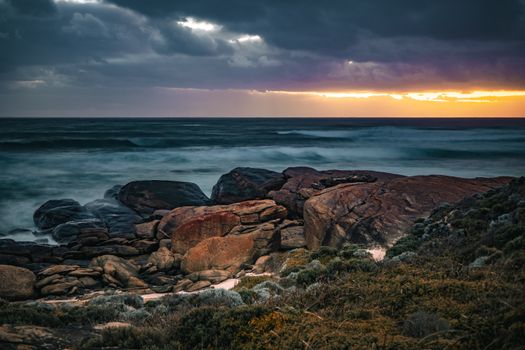 Breathtaking view of ocean waves and rocky shoreline at sunset in Redgate, Western Australia, showcasing vibrant colors and dramatic clouds.