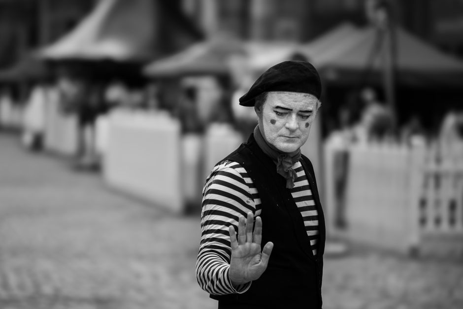 Engaging black and white photo of a mime artist in a street performance, striking a contemplative pose.