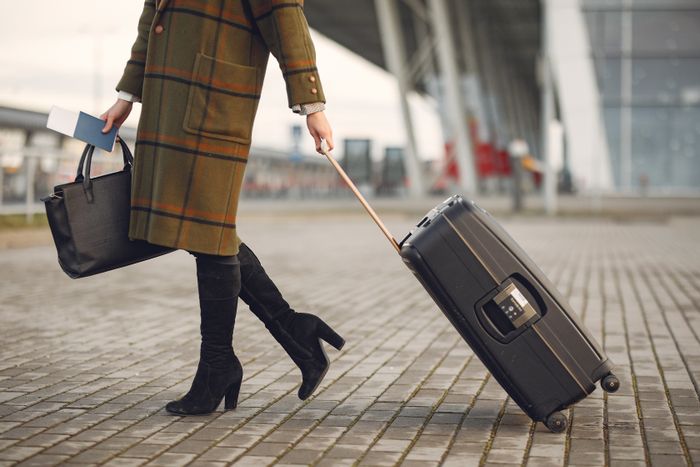 Mulher elegante com mala caminhando perto de terminal moderno