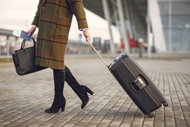 Stylish Woman With Suitcase And Bag Walking On Street Near Modern Airport Terminal