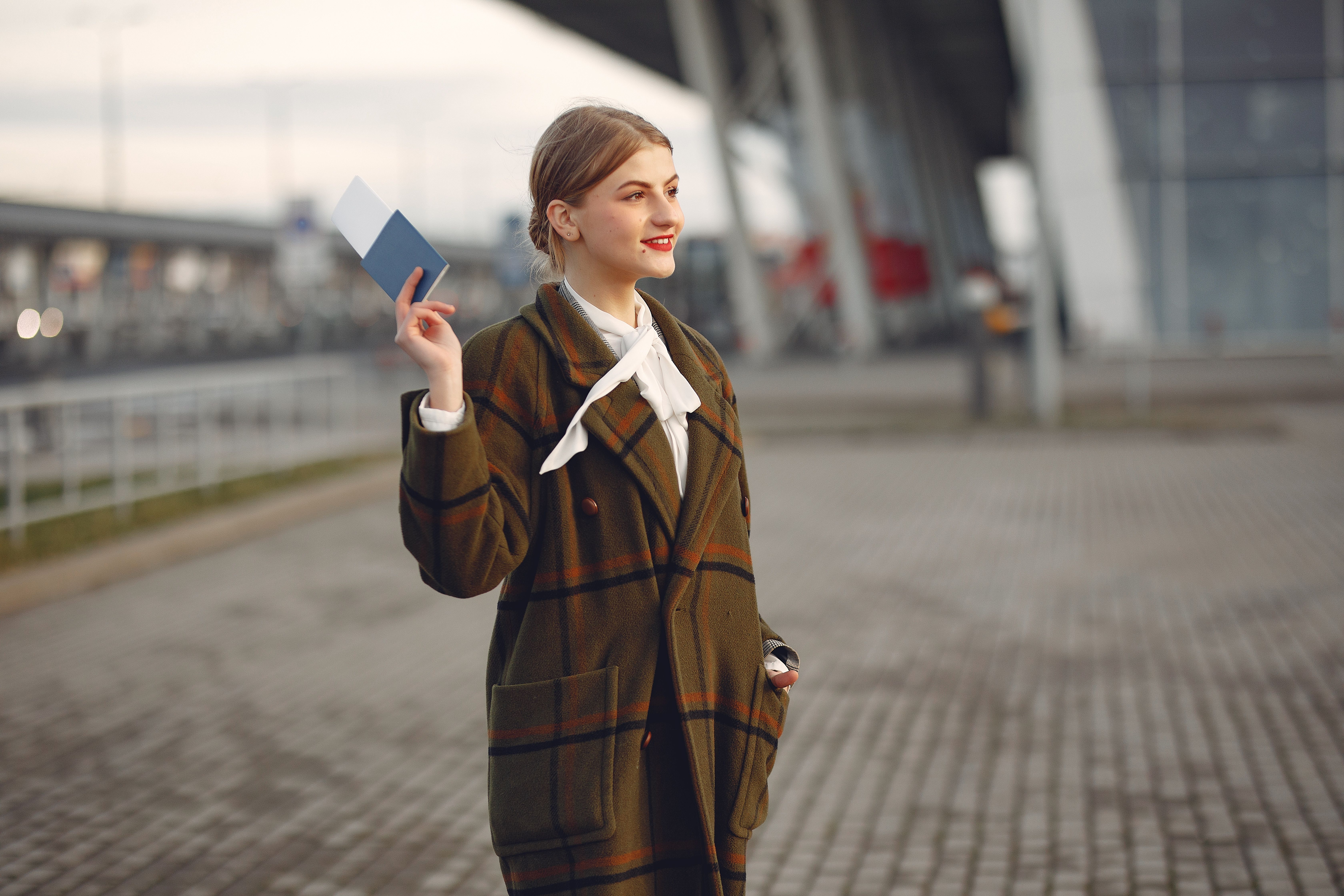 Lächelnde junge Frau mit Reisepass und Flugticket vor einer Universität