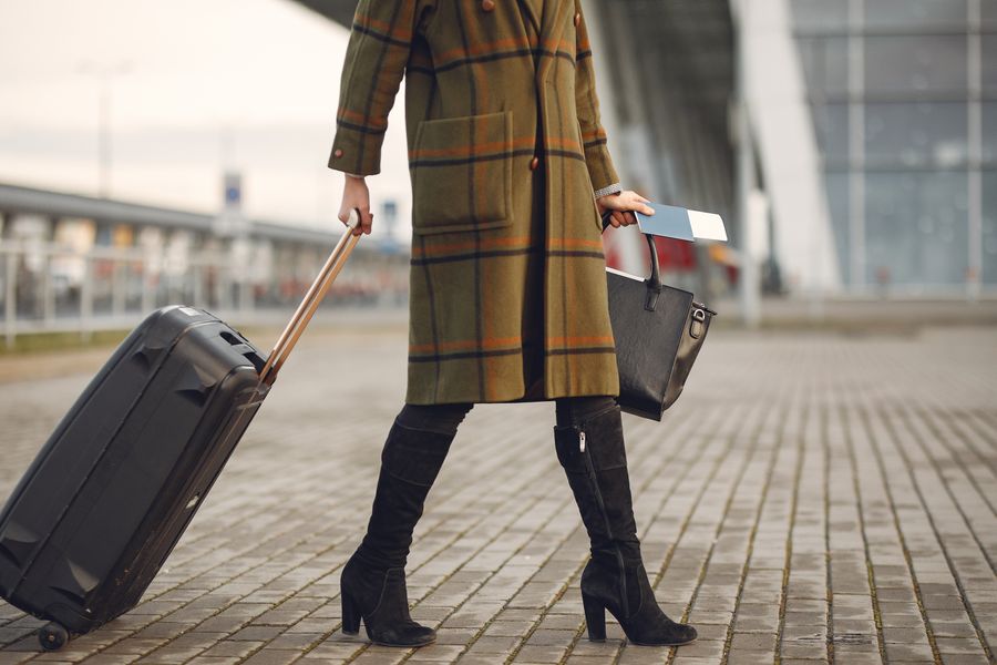 Stylish woman pulls suitcase at airport, ready for travel.