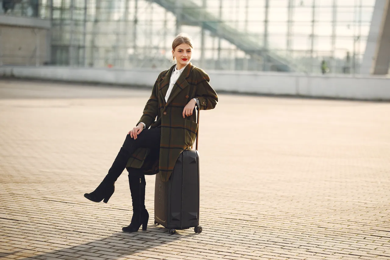 plaid-coat-suitcase-airport-look Woman in a plaid coat sitting on her suitcase at the airport