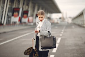 Worried young businesswoman with suitcase hurrying on flight on urban background
