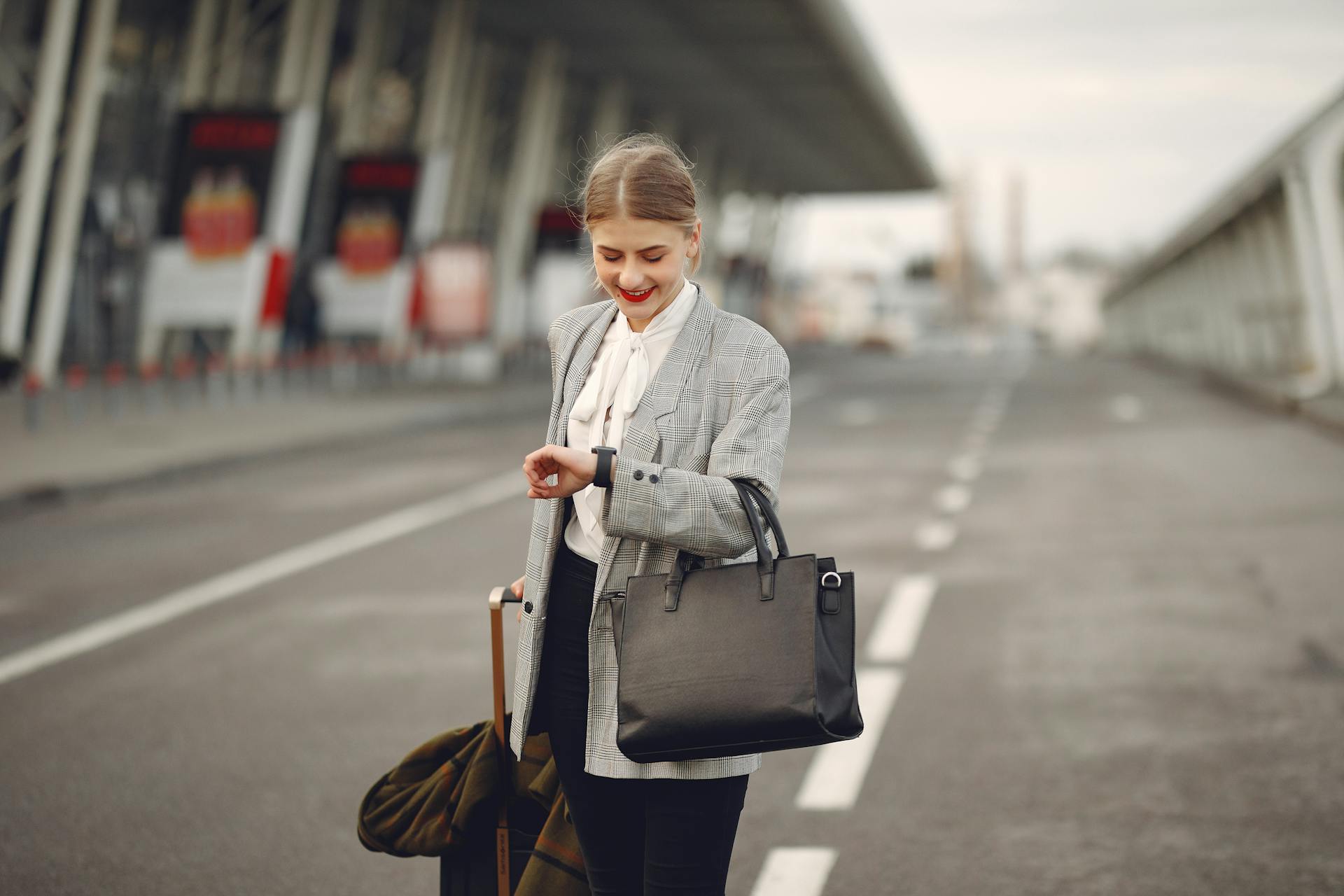 Professional woman with luggage at outdoor airport terminal checking time on wristwatch.