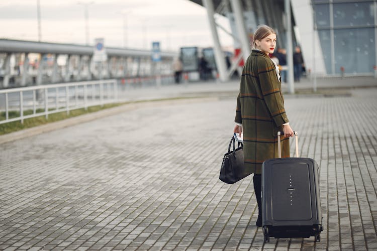 Back View Of Trendy Businesswoman Carrying Baggage Before Flight Near Airport Building