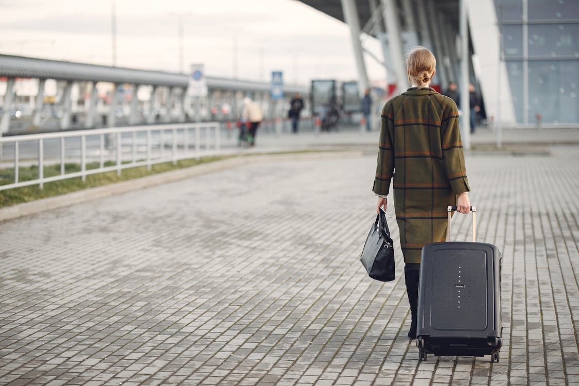 Free Unrecognizable woman with suitcase walking near airport terminal Stock Photo