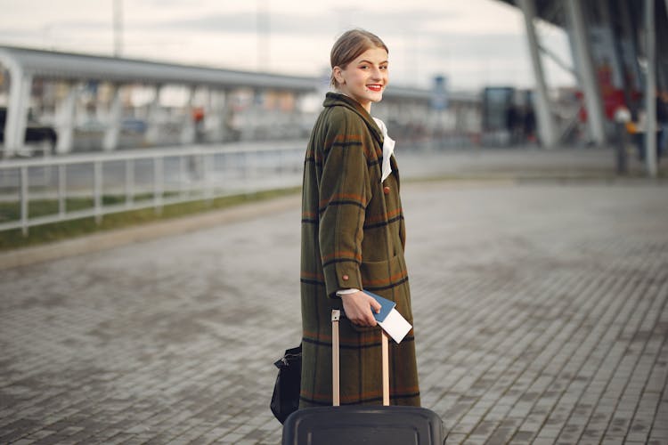 Smiling Female Traveler Walking With Suitcase And Passport Near Train Station