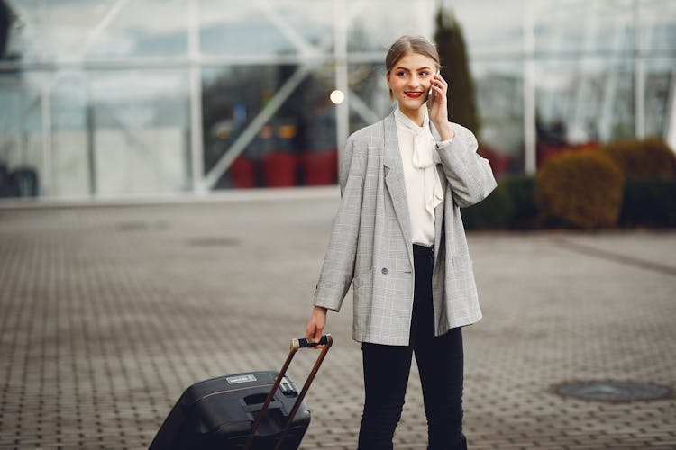 Stylish Businesswoman Speaking On Smartphone While Standing With Luggage Near Airport