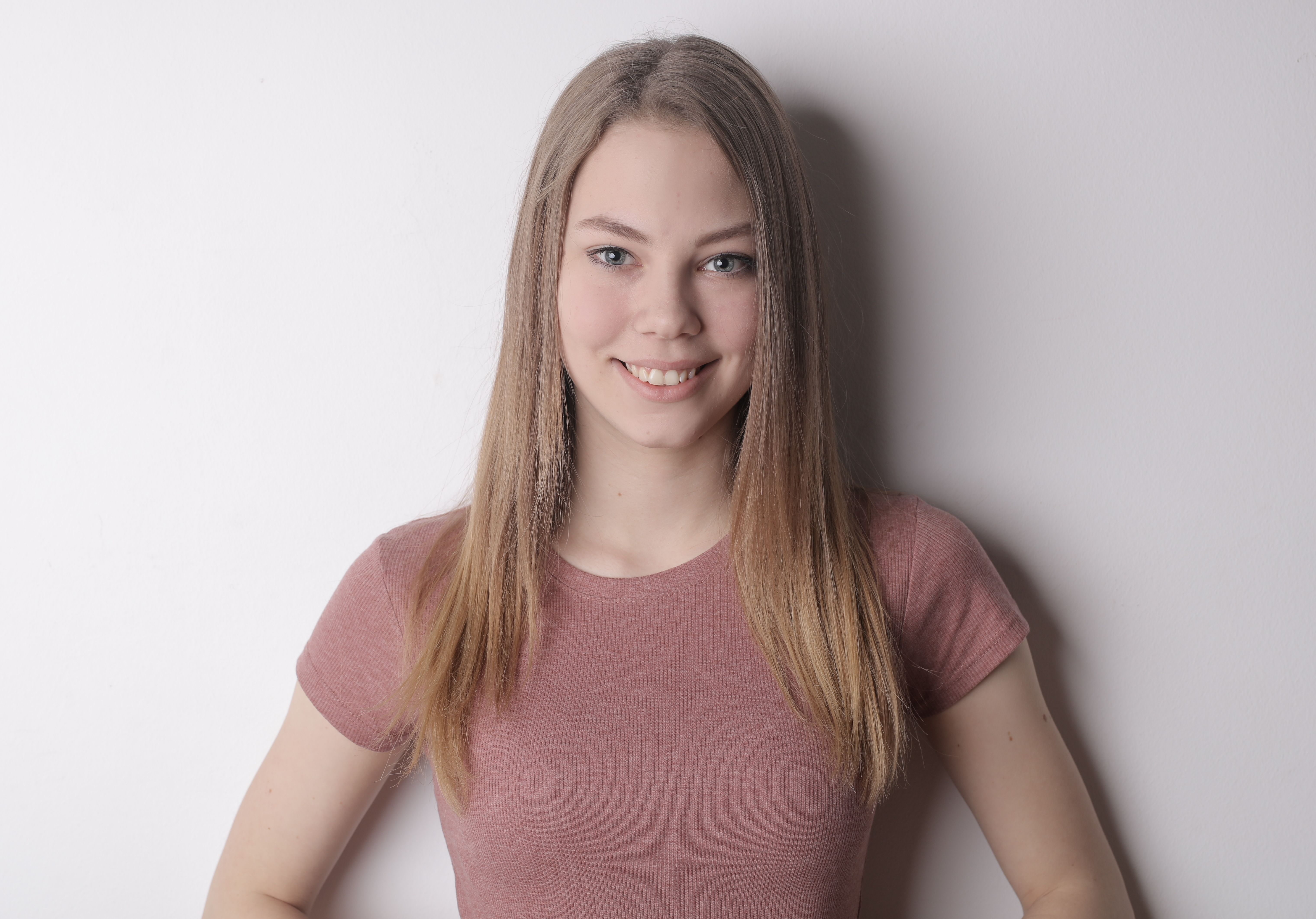 Portrait of a young woman with long hair smiling against a white background.
