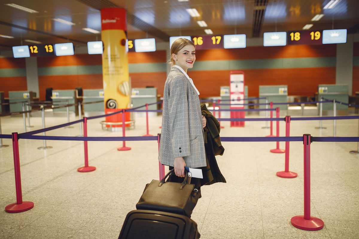 Traveller with a rolling suitcase walking past a row of empty numbered check-in desks at an airport terminal