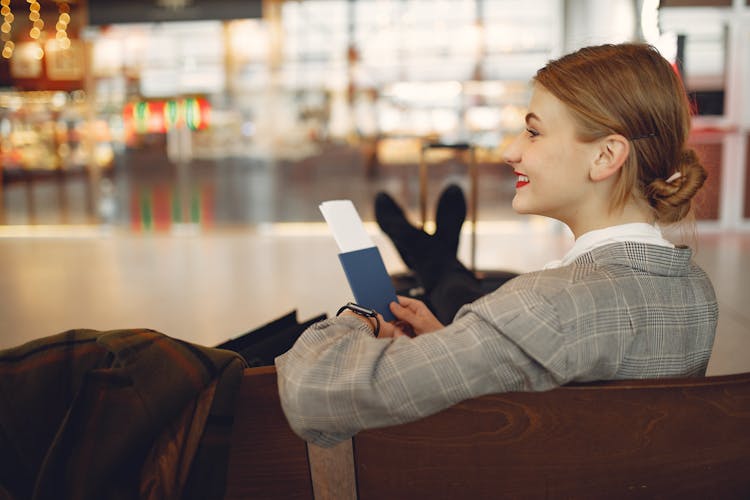 Happy Young Woman Waiting For Flight And Relaxing In Waiting Area Of Airport