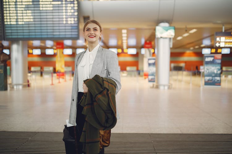 Happy Young Woman Standing With Baggage Near Departure Board In Airport