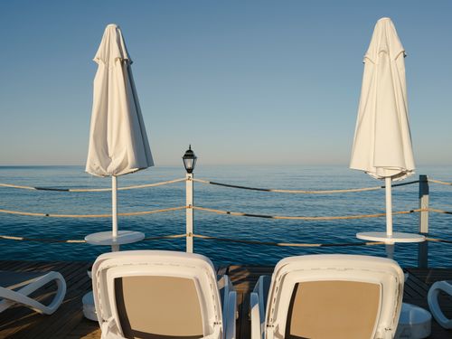 Free Tranquil seaside deck with sunbeds and umbrellas under a clear blue sky, perfect for a summer vacation. Stock Photo