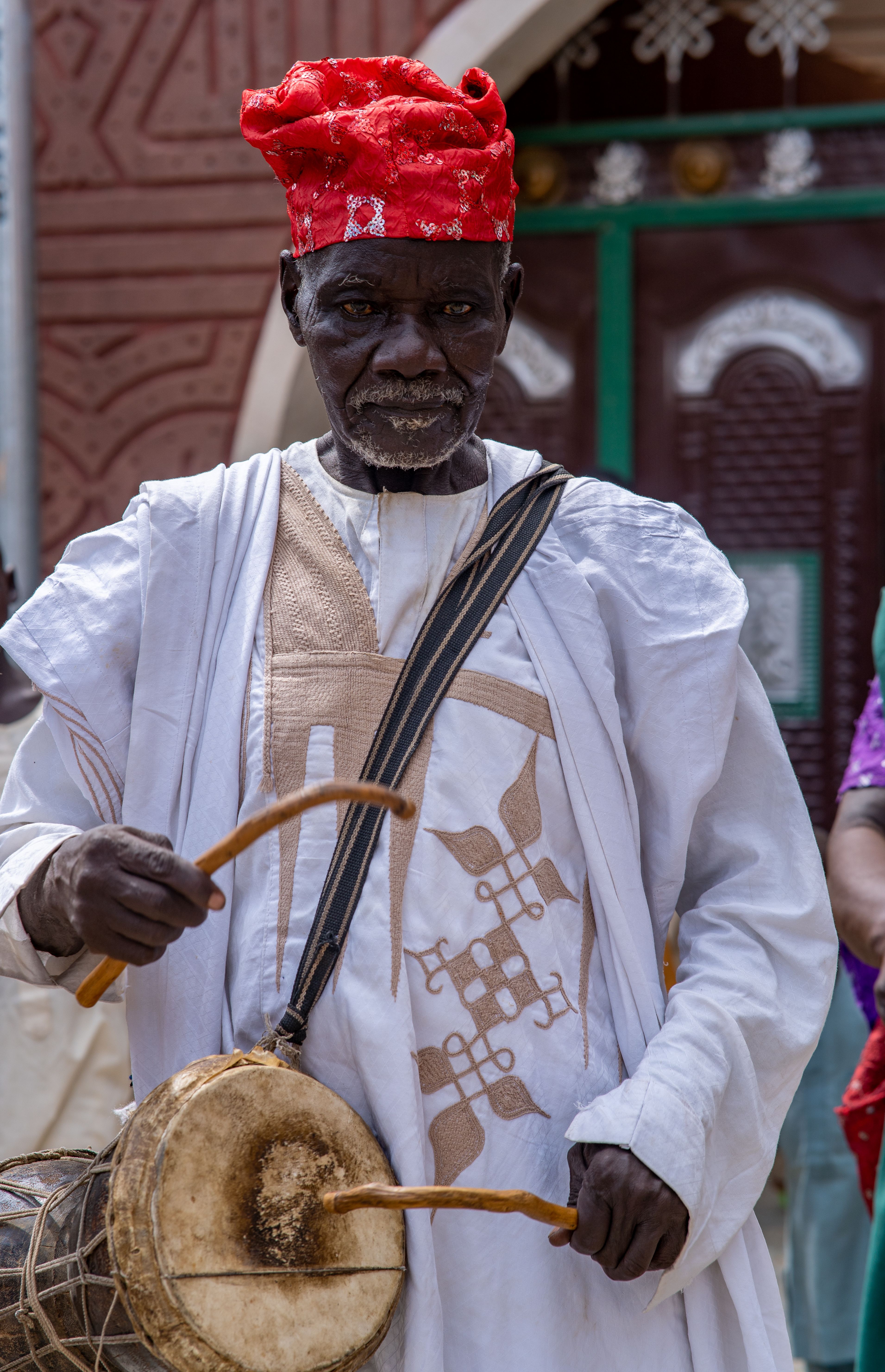 Elderly Nigerian man in red hat playing traditional drum in Rano, Nigeria.
