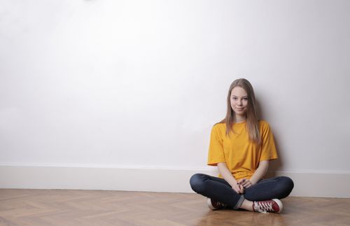 Free Portrait of a young woman in yellow casual wear sitting on the floor with a relaxed smile indoors. Stock Photo