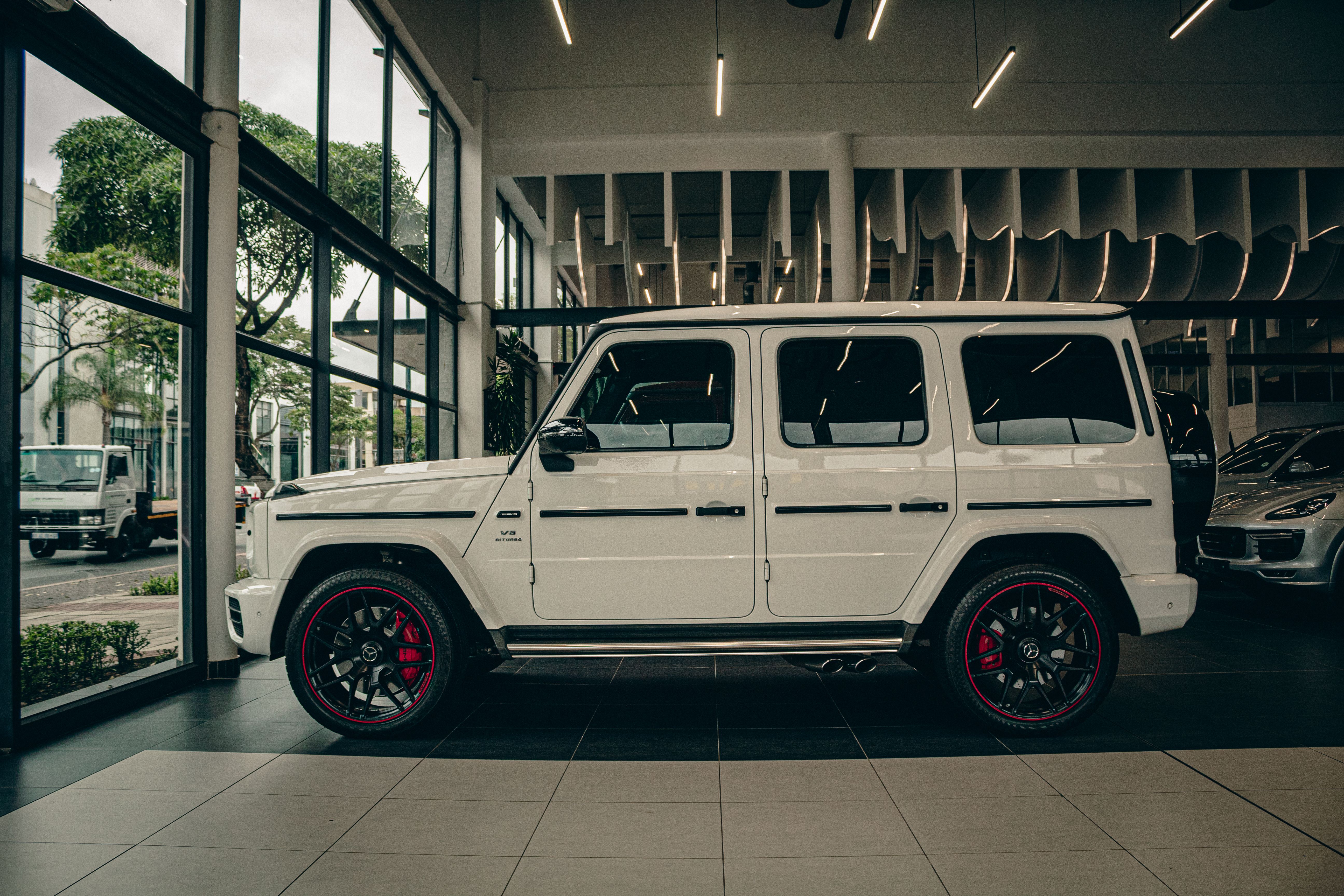 White luxury SUV on display in a modern car showroom with glass walls and stylish interior lighting.