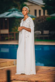 Elegant woman in a white dress standing by a pool in Nairobi, Kenya. Perfect for cultural and fashion themes.
