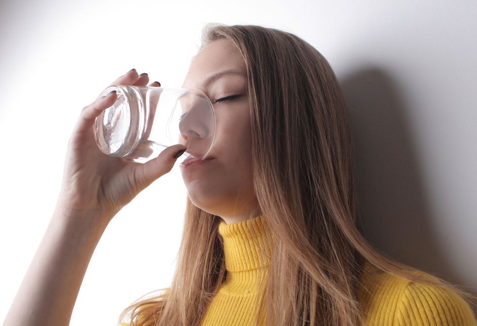 Woman in a yellow sweater drinks water from a transparent glass.