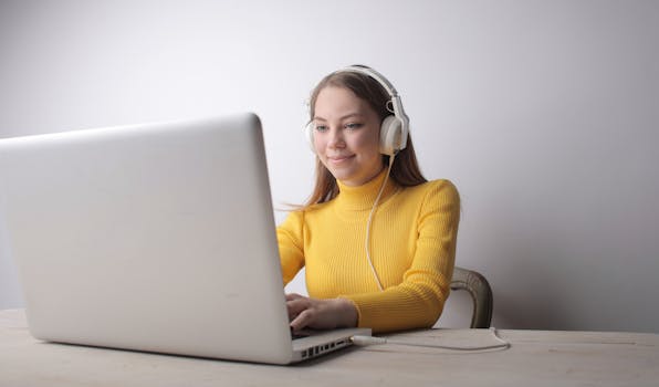 Smiling woman in yellow sweater working on a laptop with headphones, representing remote work.