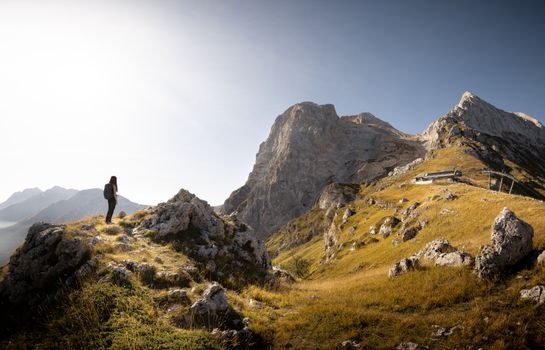 A lone hiker stands amidst rocky terrain with majestic mountain views under a clear sky.