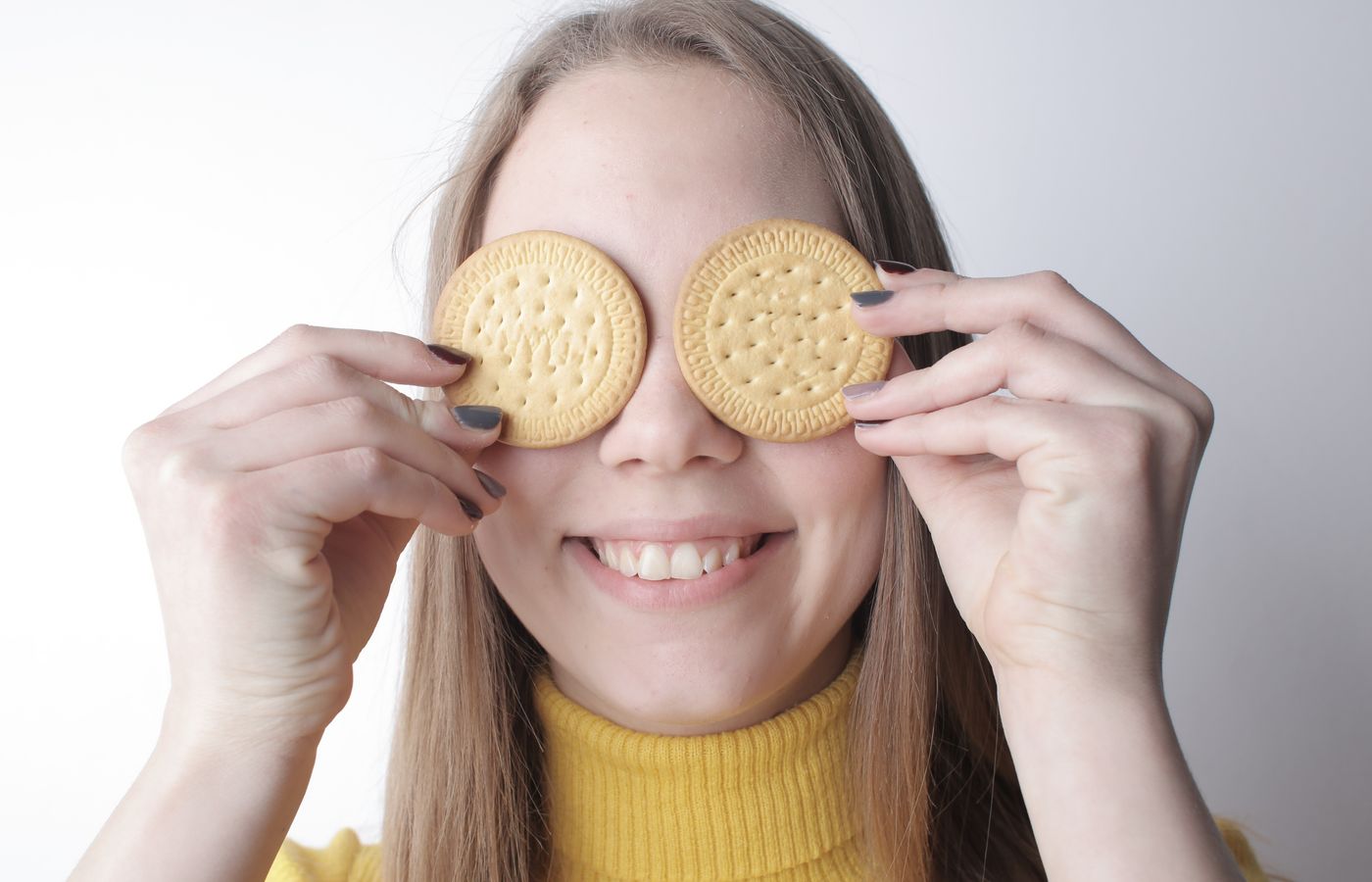 A happy young woman playfully holds cookies over her eyes, creating a joyful and fun mood.