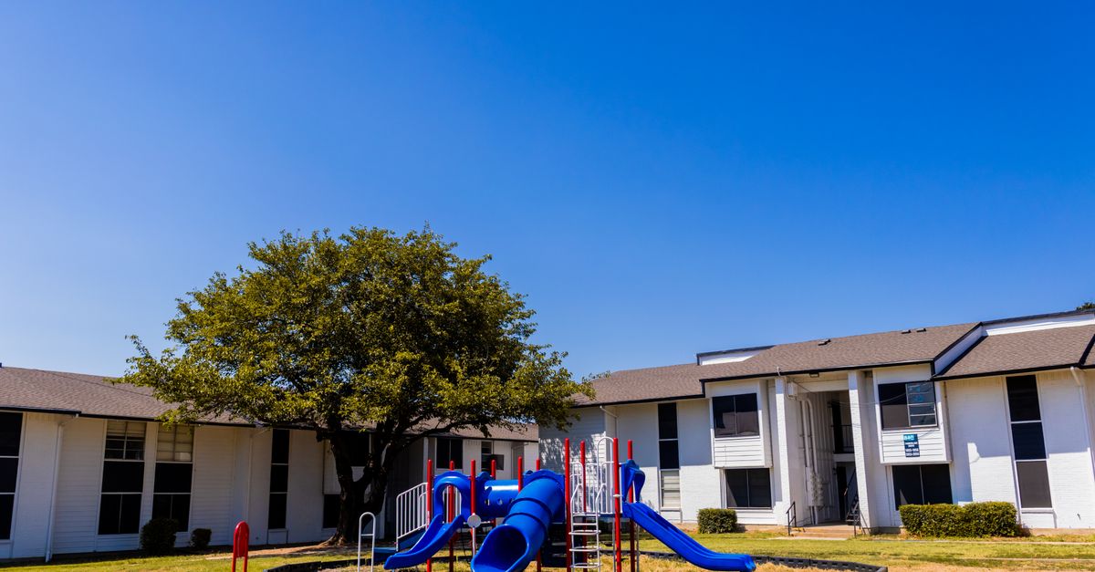 Outdoor playground with blue slides in a suburban residential area under clear blue skies.
