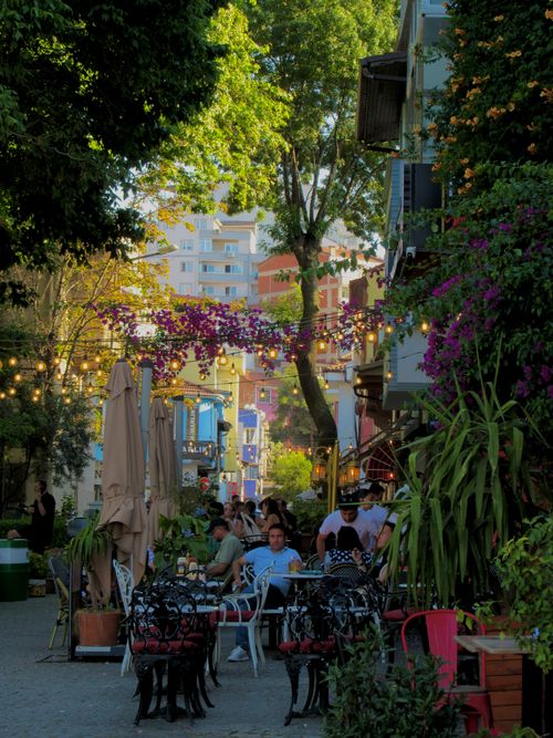 Free Bustling outdoor cafe scene with lush foliage and vibrant ambiance in a cityscape. Stock Photo