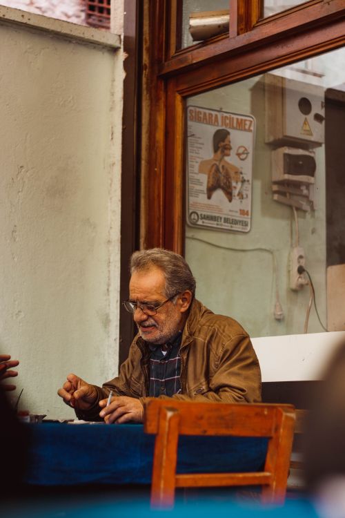 Free Elderly man in casual attire enjoying a coffee at an outdoor cafe table. Stock Photo
