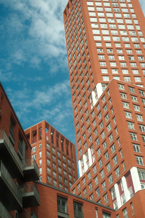 Free A view of modern red brick skyscrapers reaching towards a clear blue sky, showcasing urban architecture. Stock Photo