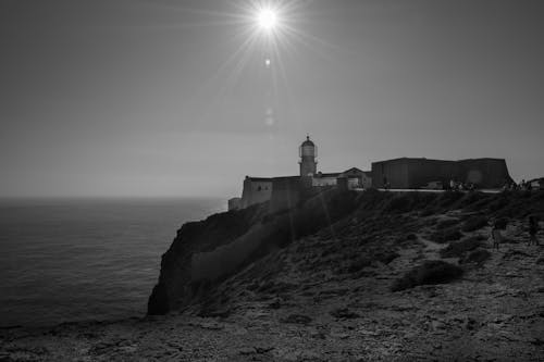 Grayscale Photo of Lighthouse Near Body of Water