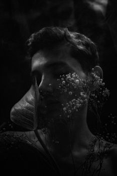 A moody black and white portrait with floral elements and soft lighting.