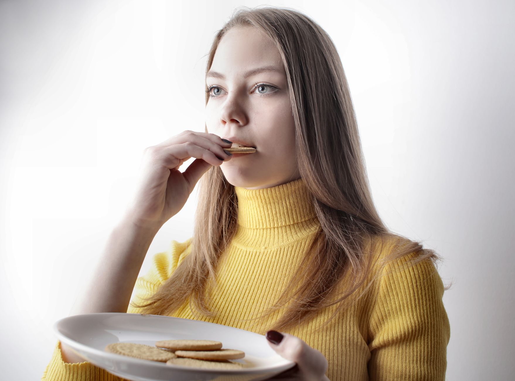 Portrait of a young woman in a yellow sweater savoring cookies indoors.