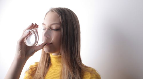 Woman In Yellow Knit Sweater Drinking from Clear Glass 