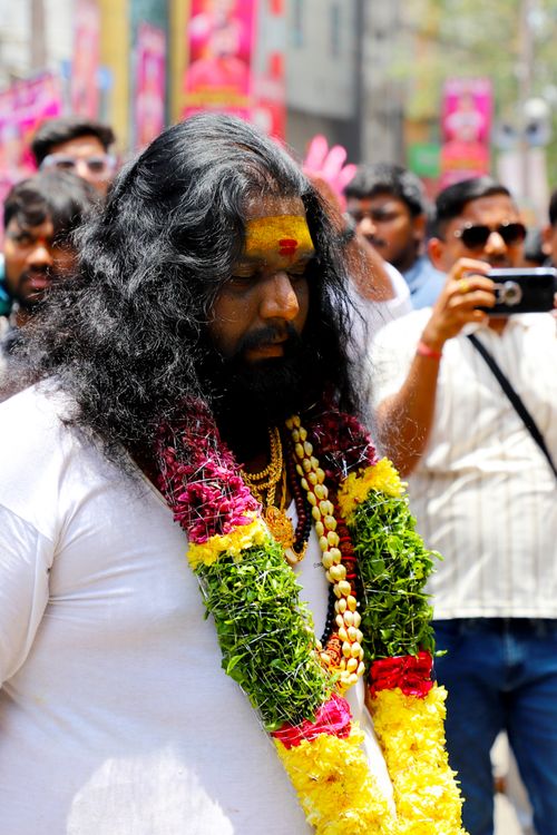 Free A cultural festival procession with a man wearing vibrant flower garlands, surrounded by a crowd. Stock Photo